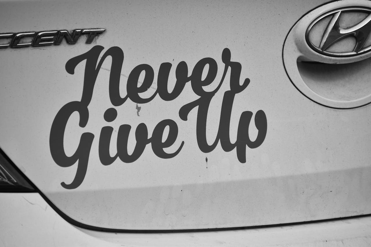 Home Black and white image of 'Never Give Up' decal on a Hyundai car.